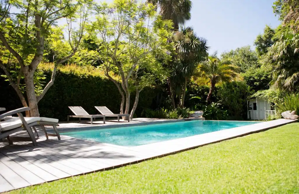 A serene backyard with a sparkling pool, surrounded by lush greenery and sun loungers under tall trees, perfect for relaxation at A Good Neighbor Property Solutions in the Tampa Bay Area, Florida