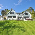 Modern house with a blue and white exterior, surrounded by a lush green lawn and gardens, set against a clear blue sky. A Good Neighbor Property Solutions in the Tampa Bay Area, Florida