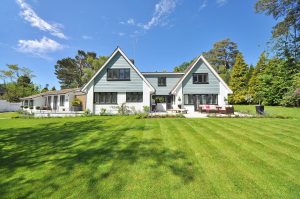 Modern house with a blue and white exterior, surrounded by a lush green lawn and gardens, set against a clear blue sky. A Good Neighbor Property Solutions in the Tampa Bay Area, Florida